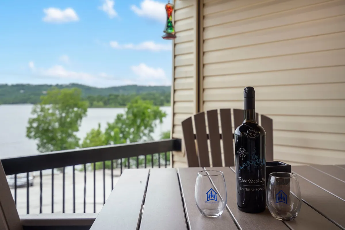 This image features a wine bottle and glasses set on an outdoor table, with a scenic view of the water in the background. The tranquil mood suggests an ideal spot for relaxing and enjoying lakeside leisure or sharing evening cocktails with friends.