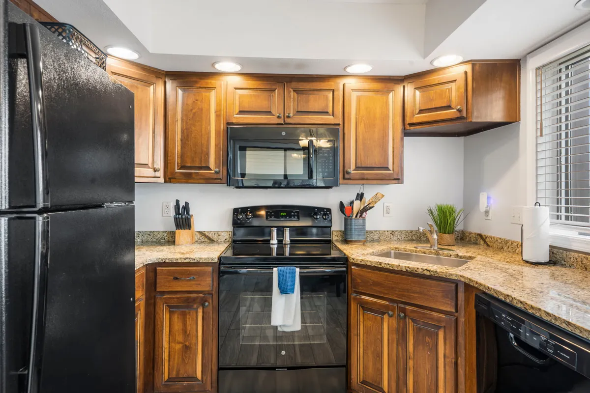 A warm and cozy kitchen with granite countertops, dark wood cabinetry, and black appliances. The space is arranged for easy movement and collaboration, ideal for group cooking sessions and family gatherings.