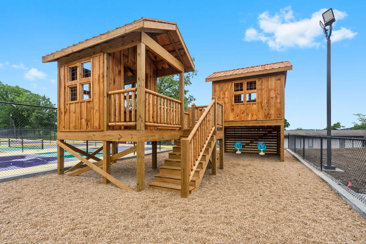 An exterior scene featuring whimsical wooden playhouses, sturdy stairs, and classic swings, with children actively climbing and swinging. The atmosphere is playful and filled with the laughter of children enjoying imaginative outdoor play.