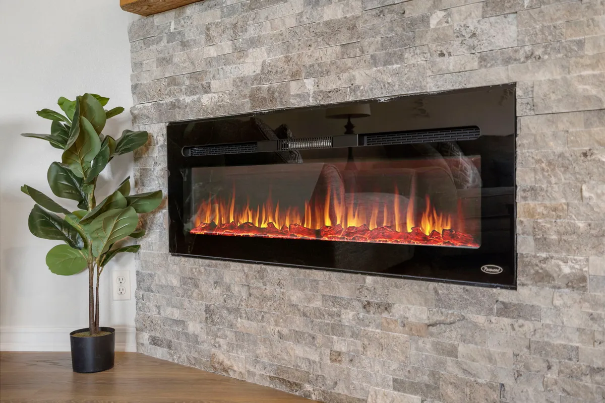 A cozy, inviting interior space featuring a striking electric fireplace set against a stone wall, complemented by greenery and comfortable seating. The area exudes warmth and relaxation, ideal for cooler seasons or unwinding after a day of exploring.