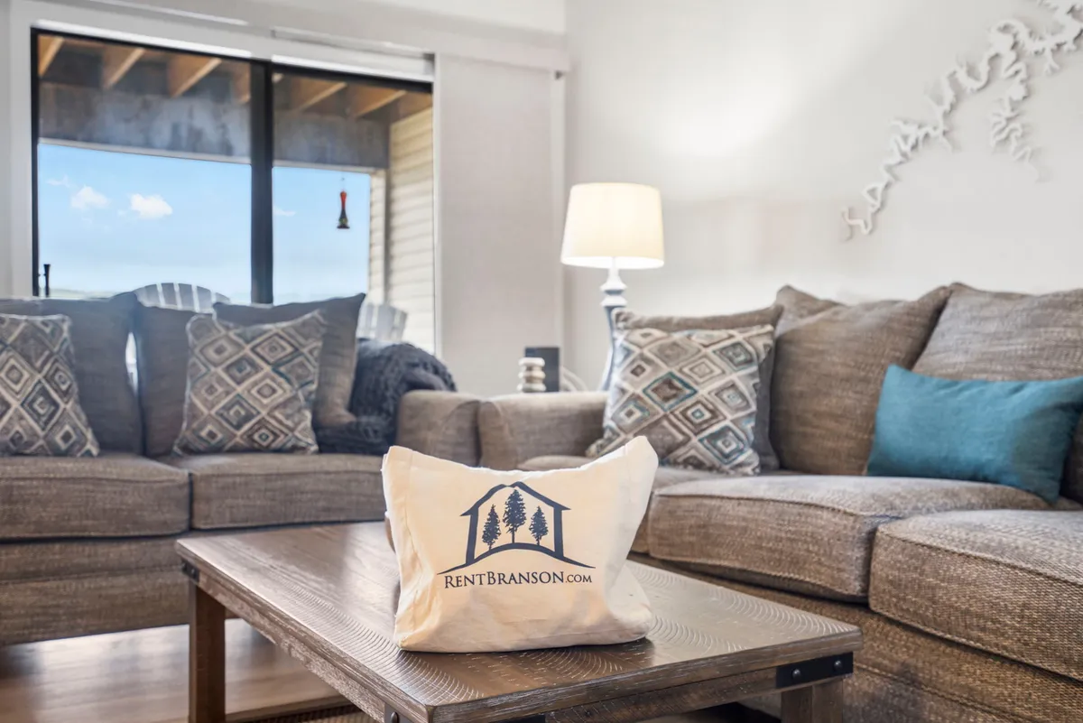 A cozy living area with a sofa, decorative pillows, coffee table, lamp, and a large window overlooking the outdoors. The inviting setup suggests a comfortable spot for guests and pets to unwind indoors while still feeling connected to the natural surroundings.