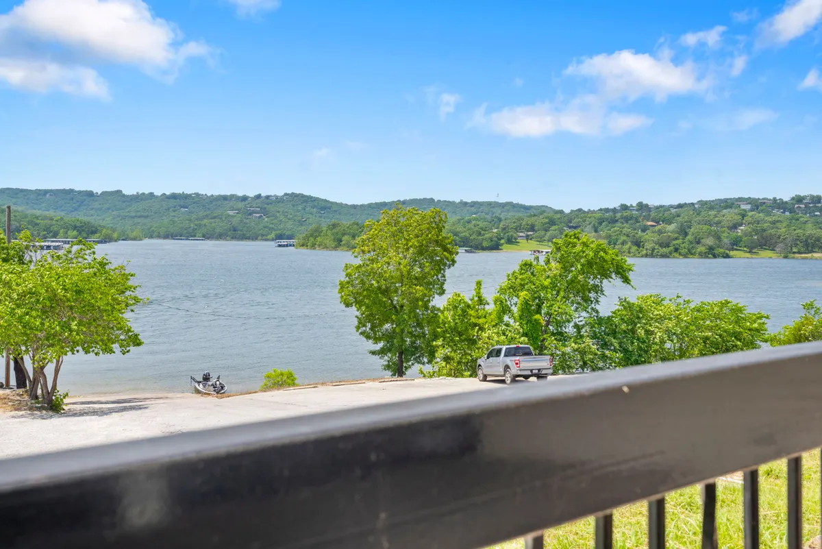 This image captures a tranquil lake bordered by trees and hills, with a boat and vehicle visible near the shore, suggesting easy lake access and outdoor activities. The view highlights the peaceful natural surroundings that guests (and their pets) can enjoy during their stay.