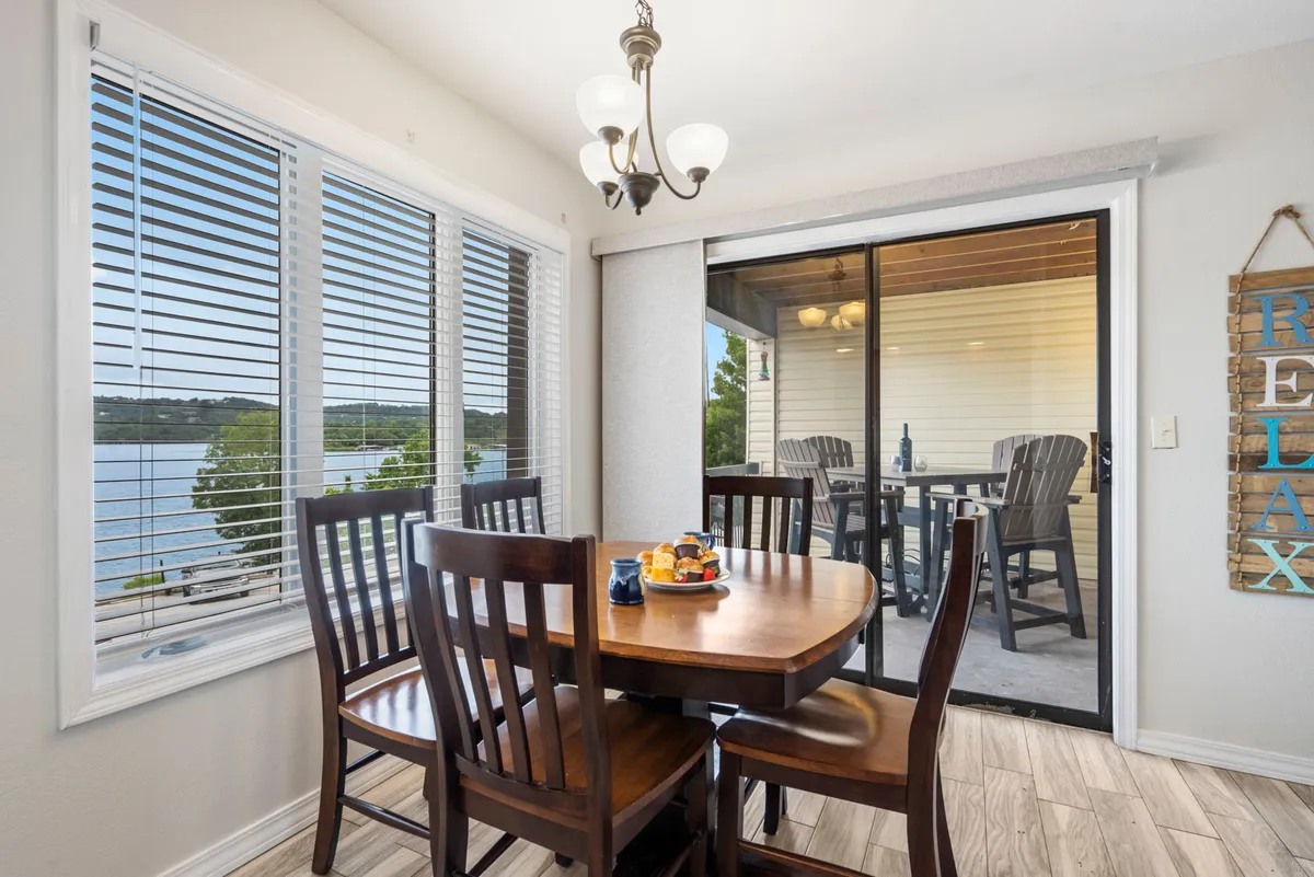 A dining table positioned near a window, offering beautiful views outside. The setting is casual and inviting, with a decorative sign adding a personal touch. The window view hints at the lakeside location, reinforcing indoor-outdoor connectivity.