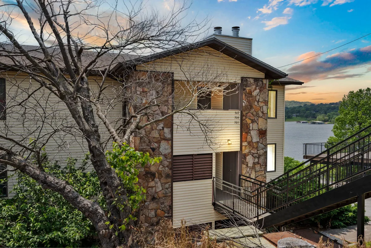 The exterior features a stone facade overlooking the water, a staircase, and tree branches framing the view—creating a welcoming space for guests to enjoy the outdoors, go for walks, or simply relax by the lakefront.