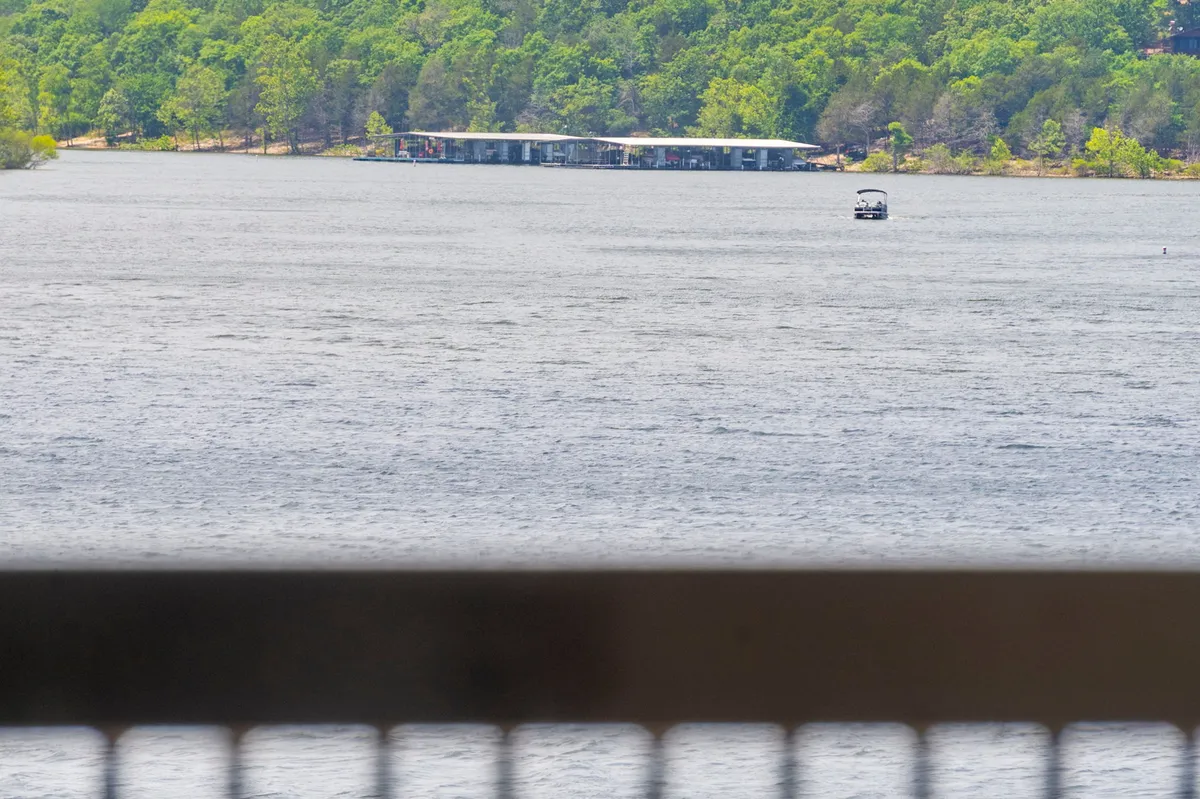 A panoramic view of Table Rock Lake with calm water, boating activity, and lush greenery surrounding a distant boat dock. The scene is serene, with clear skies and gentle ripples, inviting viewers to imagine boating, fishing, or paddle boarding.