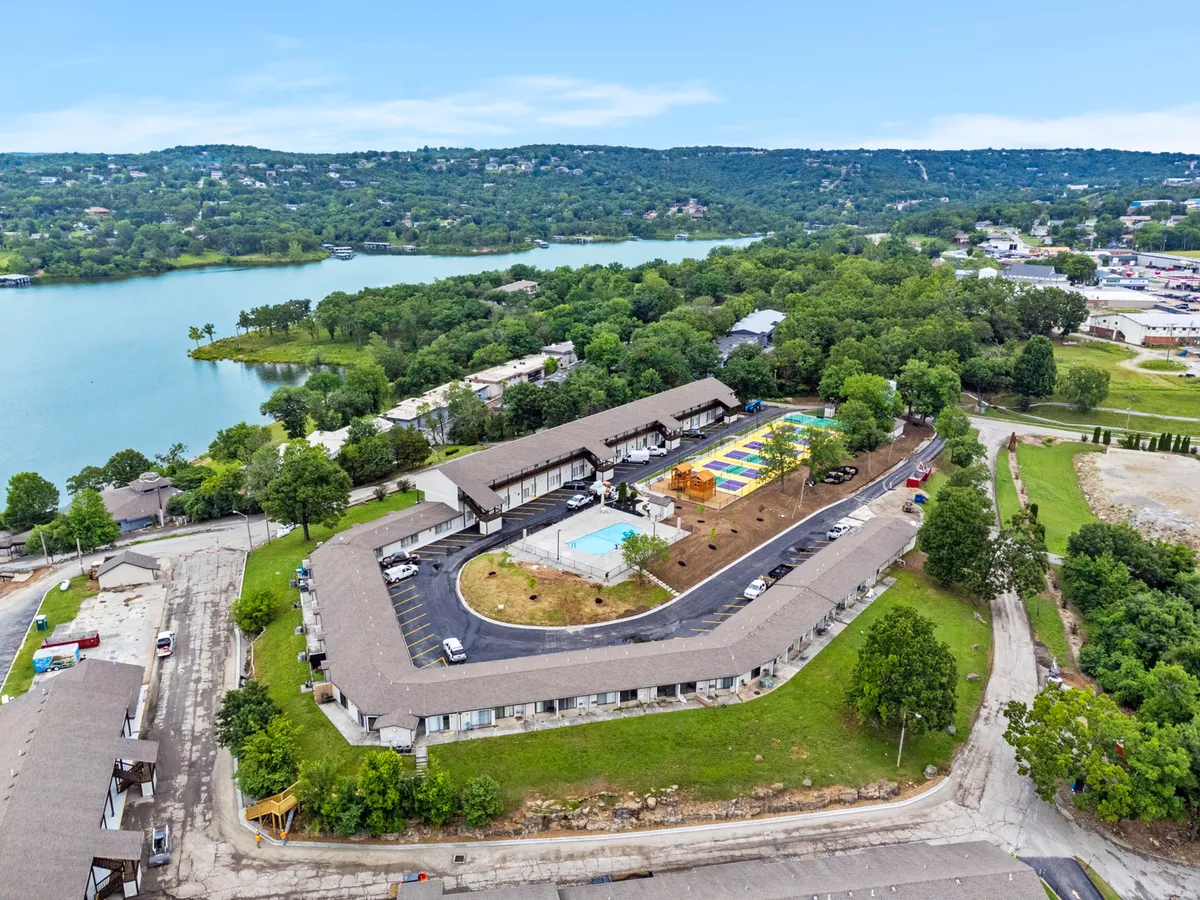 A lively exterior view capturing both a swimming pool and a colorful play area, with the scenic lake visible in the background. Children are shown playing, and families gather in the cheerful, sunlit setting, highlighting the resort's family-friendly atmosphere.
